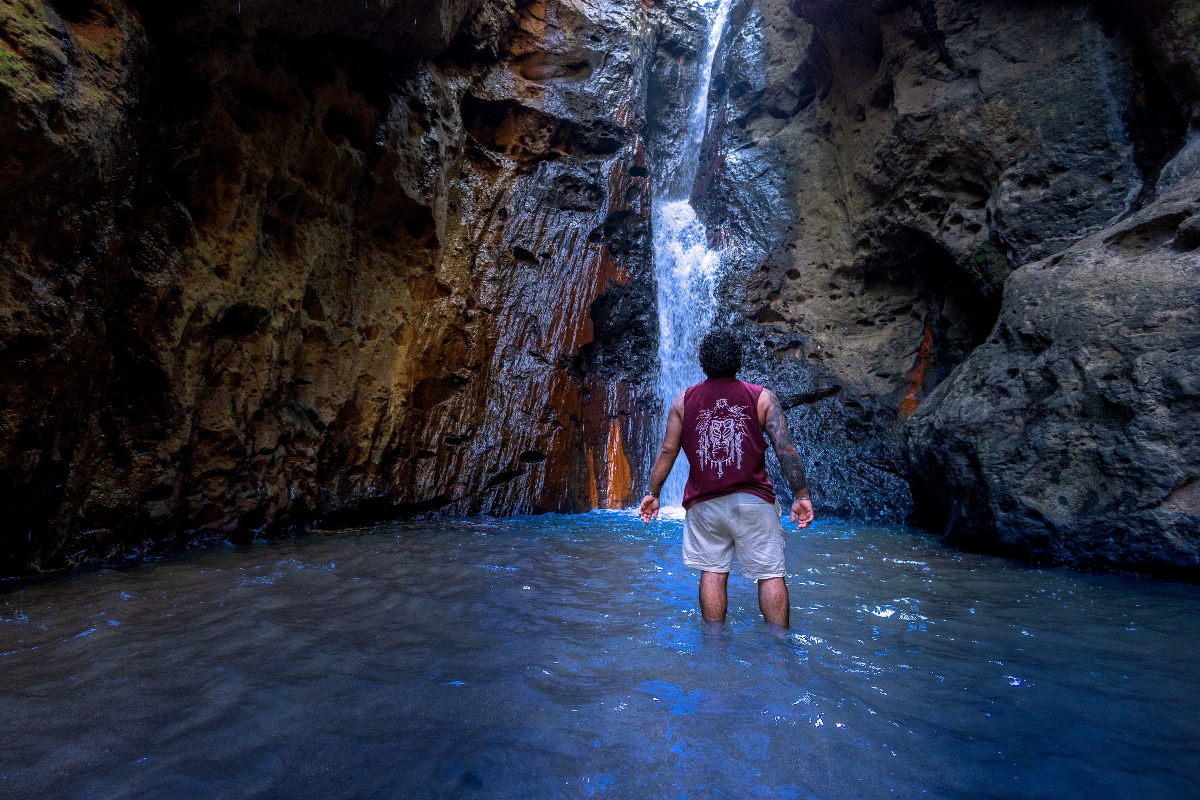 Wading into a narrow sea cave toward a waterfall cutting through the rock.