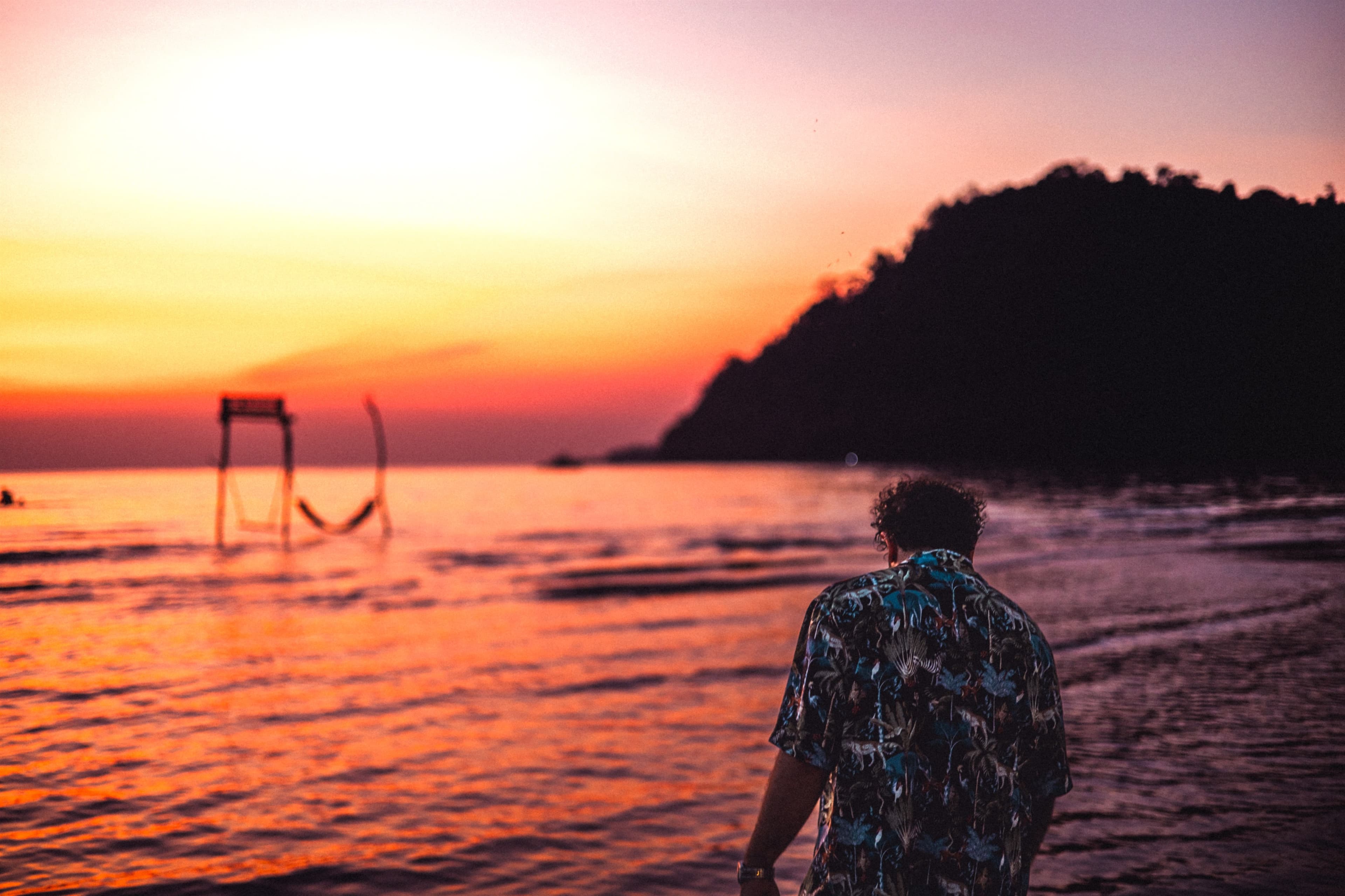 Walking the shoreline at sunset, a hammock frame standing in the shallows ahead.
