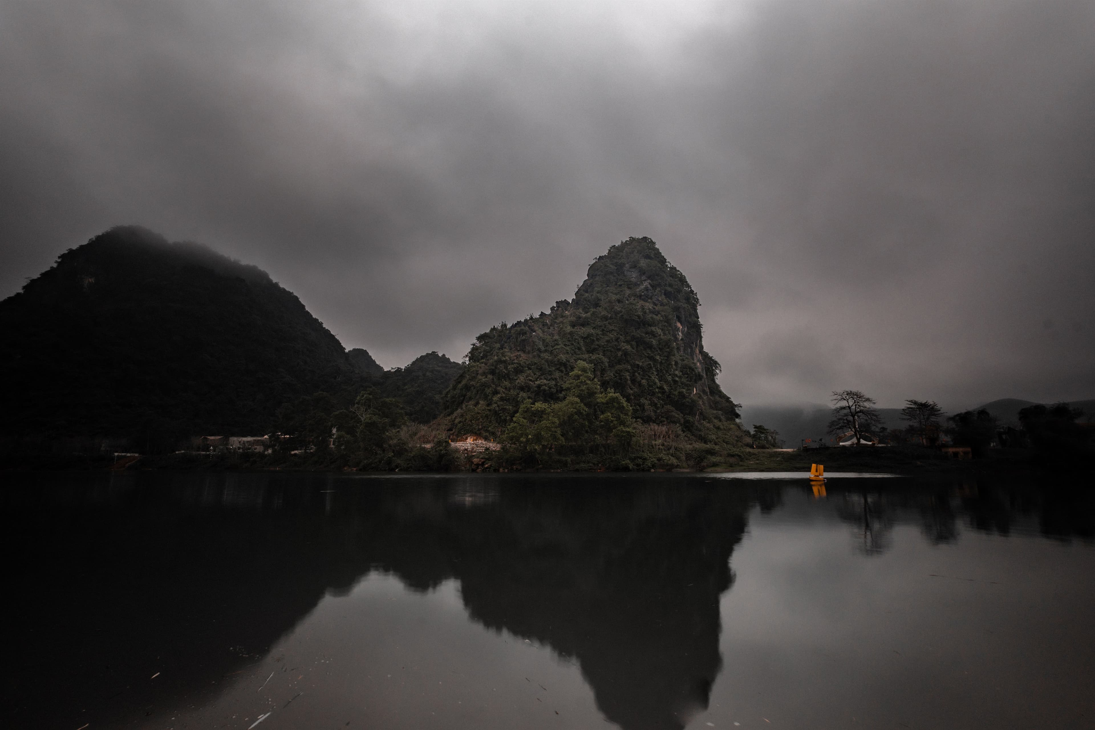 A karst outcrop and a single yellow boat mirrored in still water under a heavy grey sky.