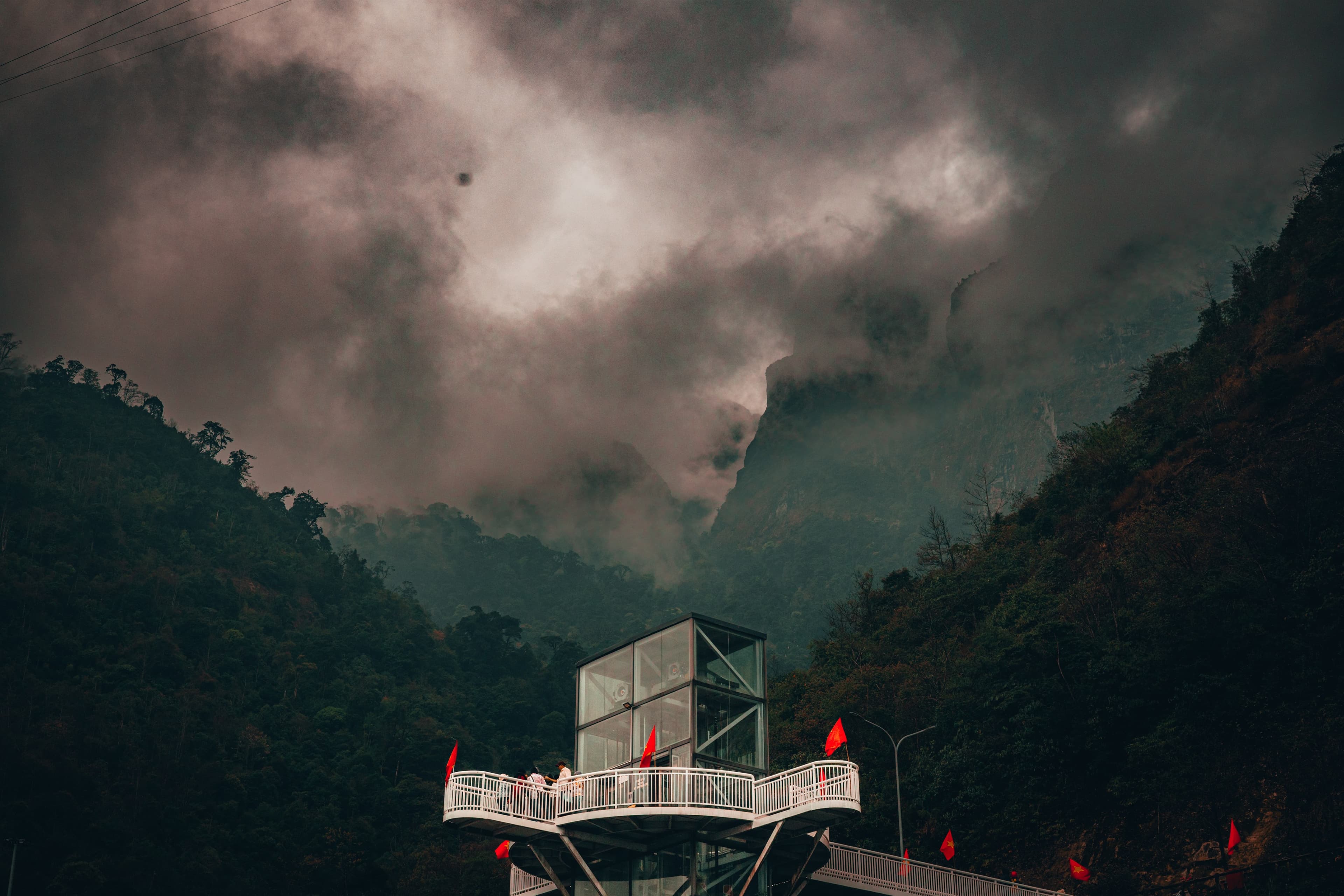 A glass viewing platform suspended over the Nho Que gorge as cloud breaks around the surrounding peaks.