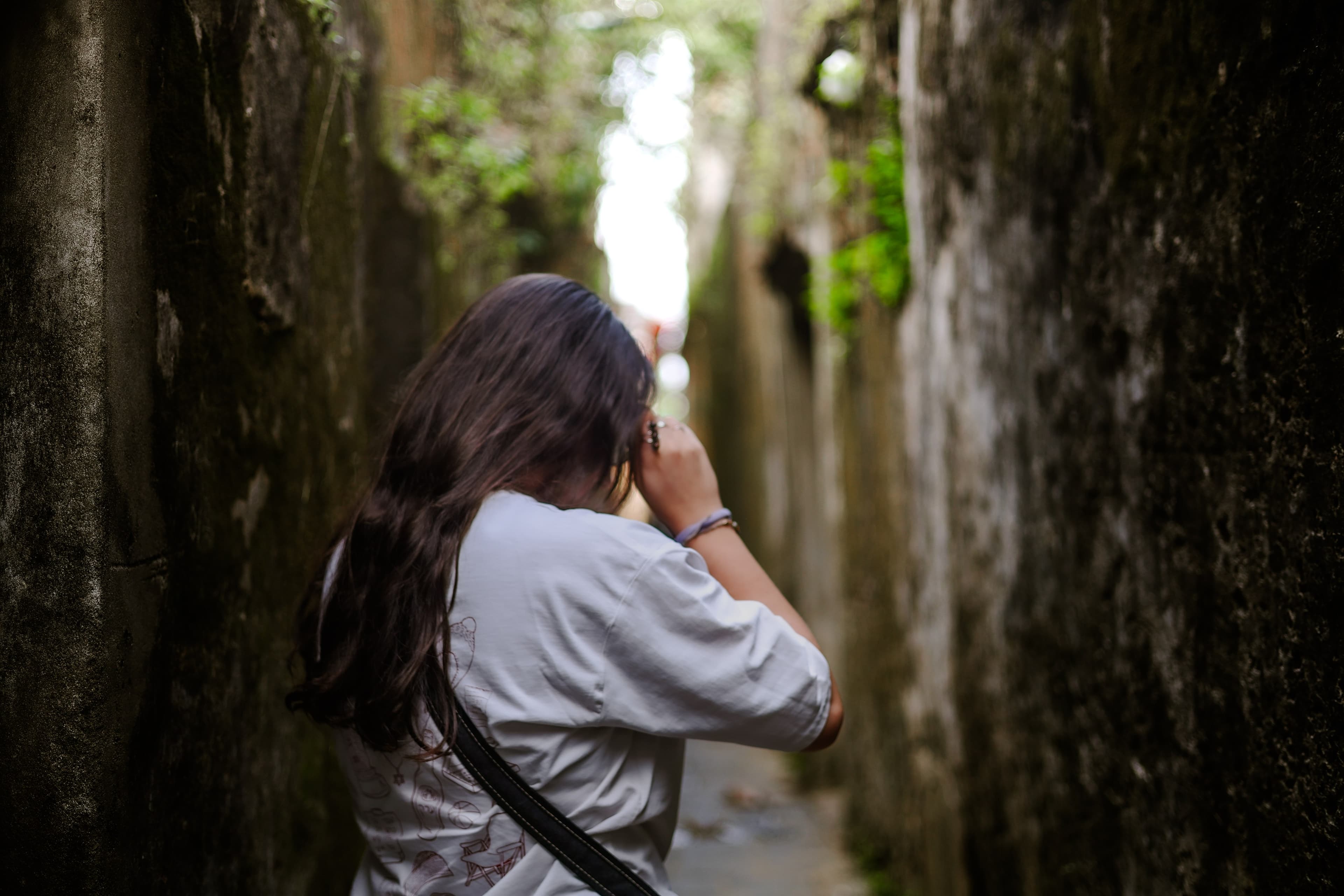 A woman photographs the view down a narrow, moss-walled alley in Ha Giang.