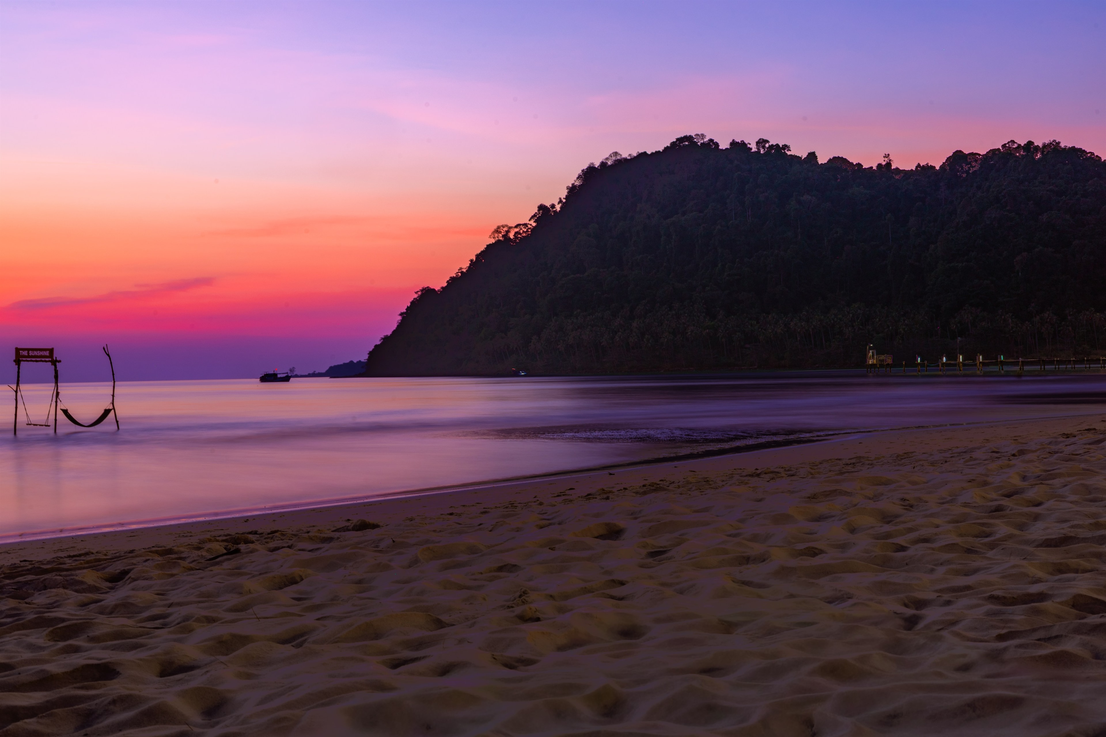 An empty swing at the waterline as the sky turns deep pink and purple over a quiet bay.