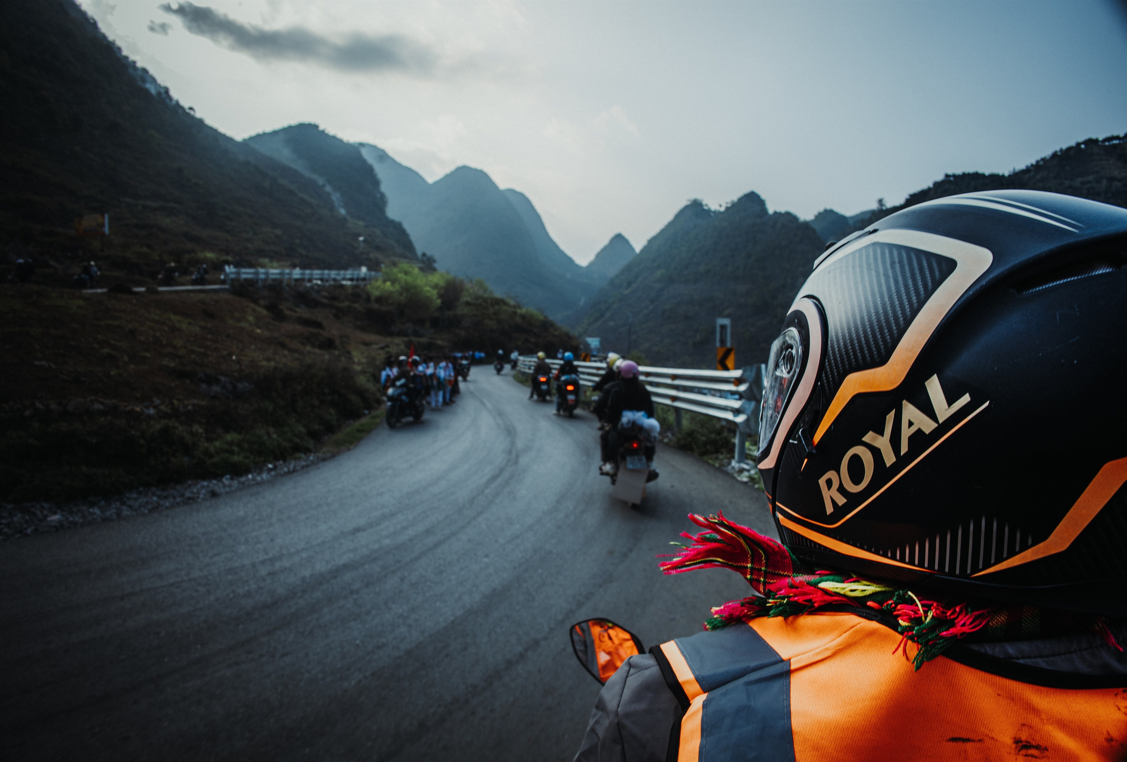 Riding the Ha Giang loop at dusk, a line of motorbikes threading the mountain road ahead.